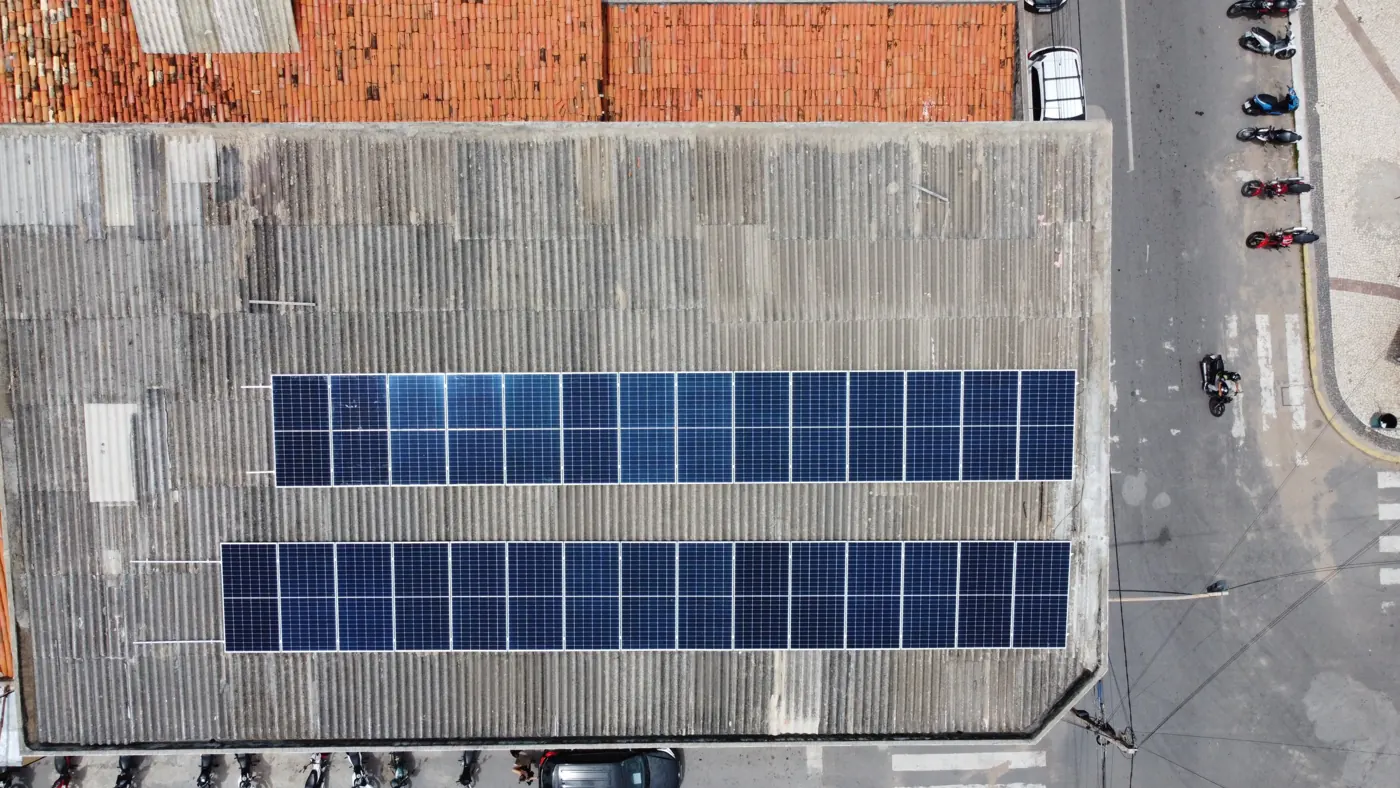 Vista aérea de duas fileiras de placas solares em telhado de telha ondulada de um prédio comercial
