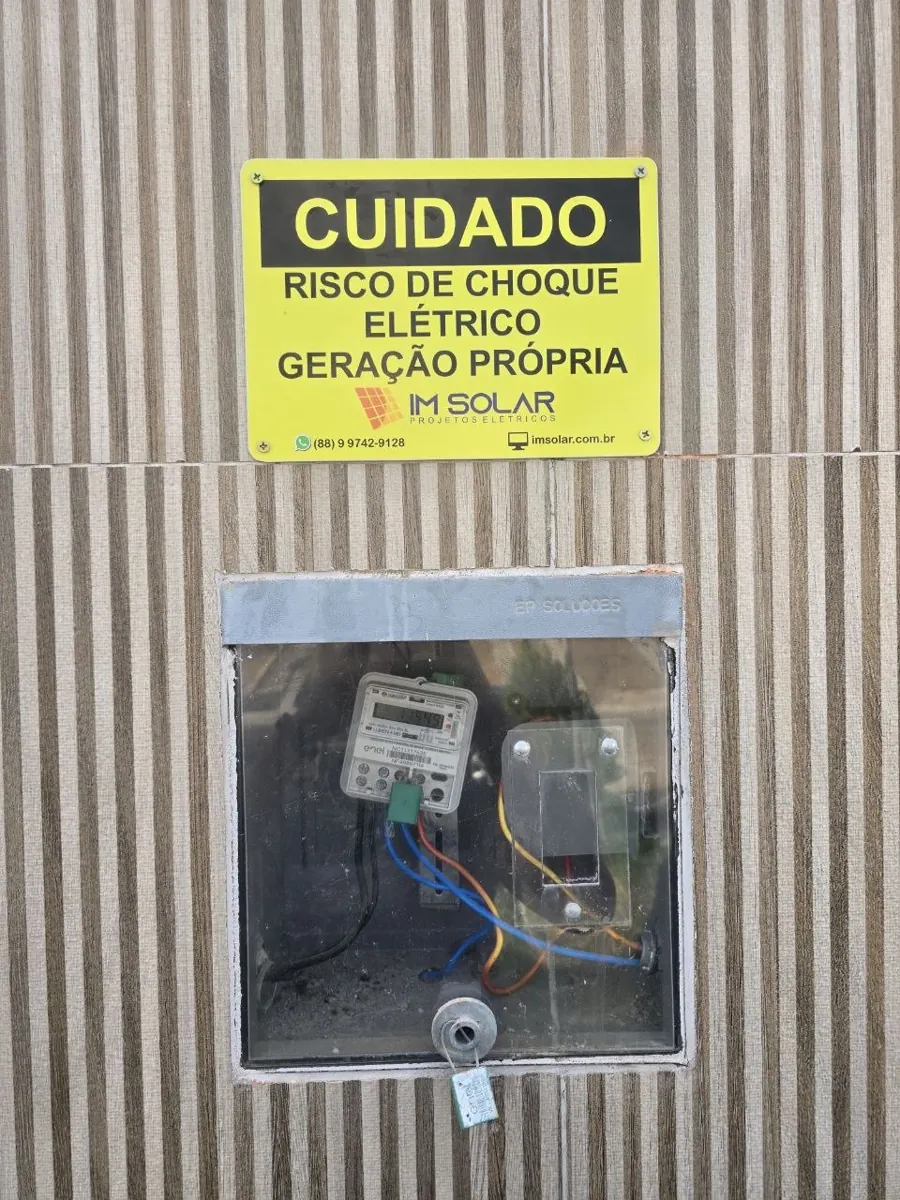 Placa de sinalização de geração própria da IM Solar ao lado do medidor da Enel instalado em muro